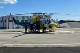 Flight crew load a stretcher into a helicopter on a hospital flight pad.