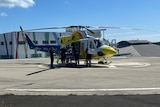Flight crew load a stretcher into a helicopter on a hospital flight pad.