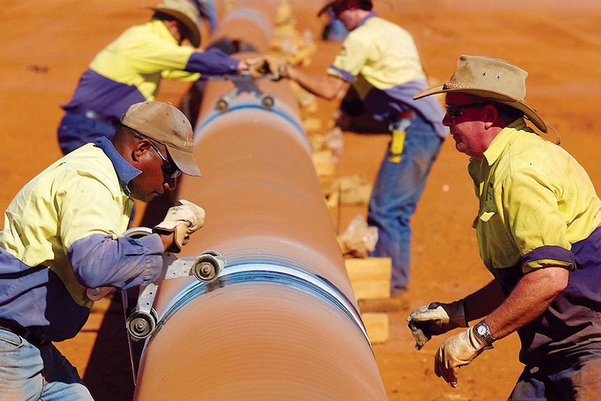 Four men work on a large pipeline in a desert
