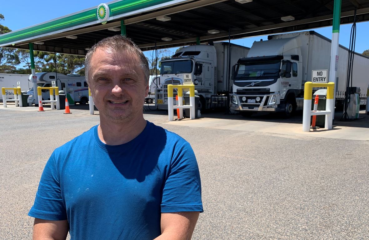 A truck driver stands in front of vehicles at a fuel station.