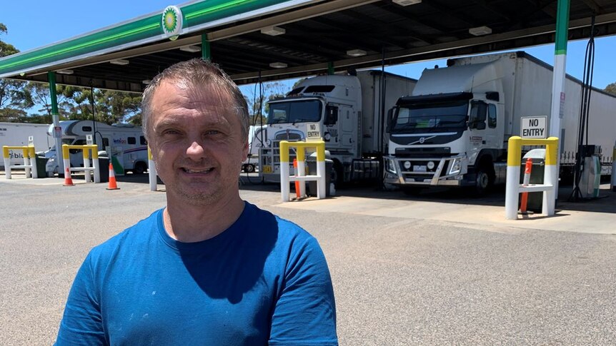 A truck driver stands in front of vehicles at a fuel station.