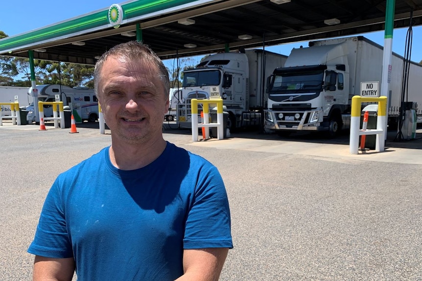 A truck driver stands in front of vehicles at a fuel station.
