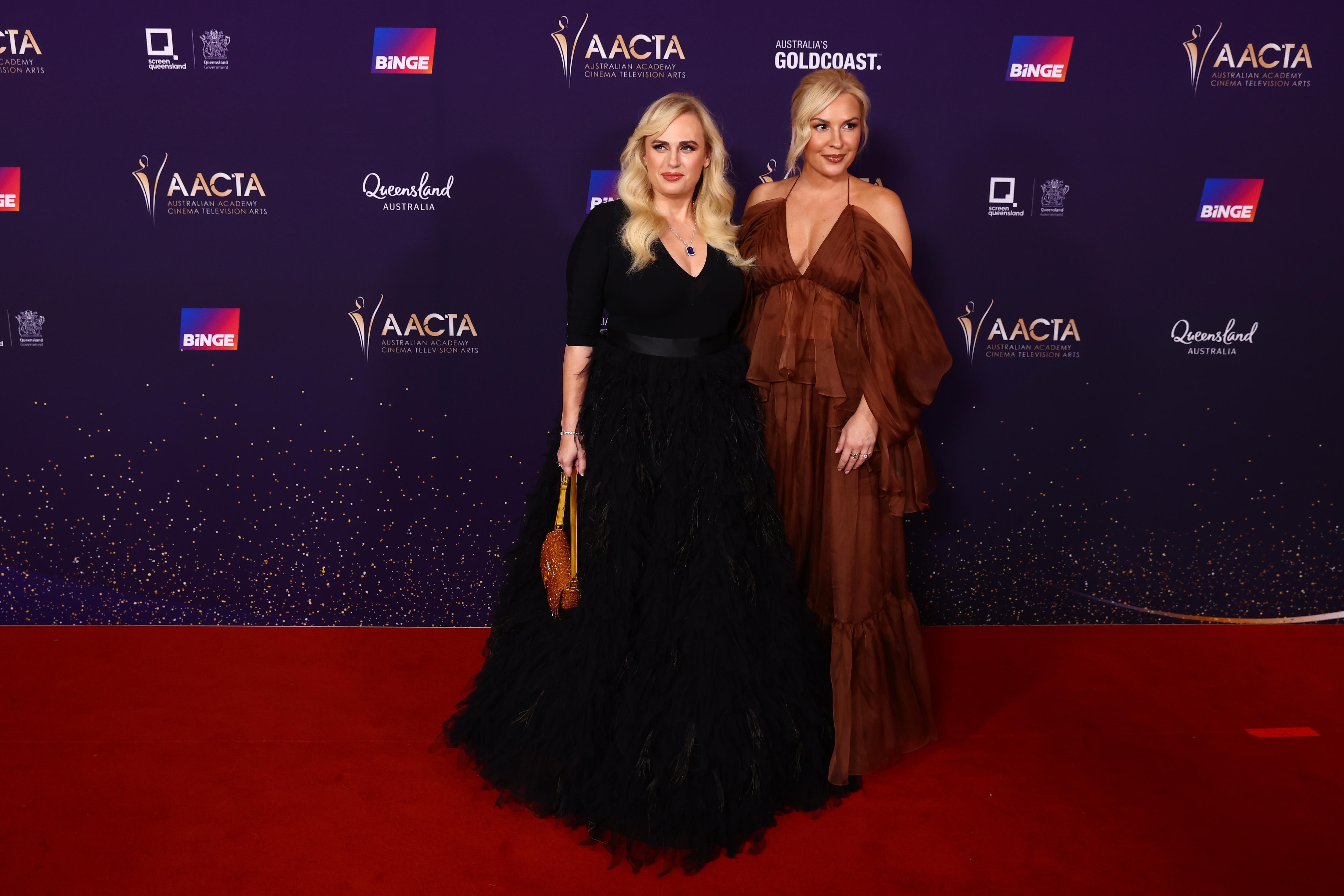 A woman in a black dress and another in a burgundy dress getting a photo on the red carpet