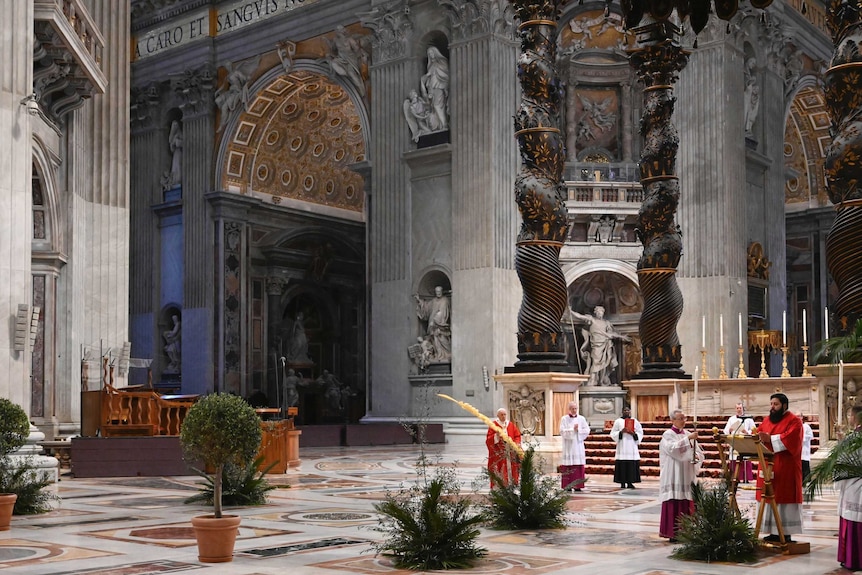 A priest speaks at a lectern while the pope watches on in an empty St Peter's Basilica.