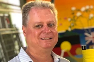 A man with grey hair with an aboriginal flag painting in the background