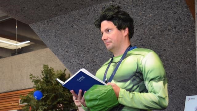 Burnie Library worker Tyron Waugh dressed as the incredible hulk, holding an open book.