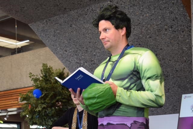 Burnie Library worker Tyron Waugh dressed as the incredible hulk, holding an open book.