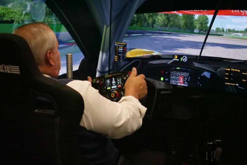 Man with white hair and shirt driving Ferrari simulator