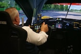 Man with white hair and white shirt driving a ferrari simulator