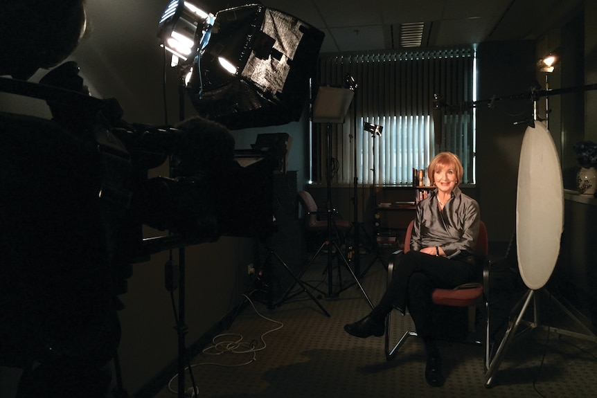 a woman with short ginger hair sits in front of cameras and lights 