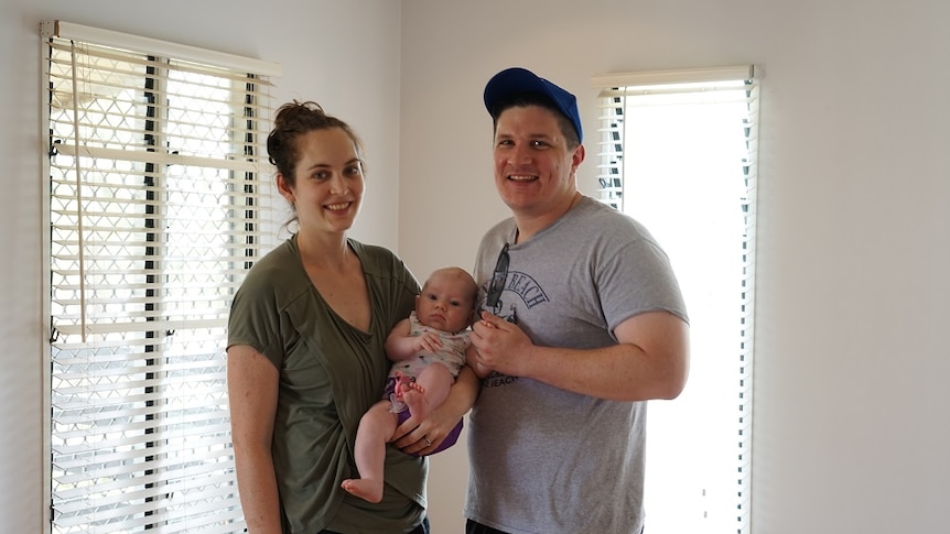 The pair stand with a baby inside the house