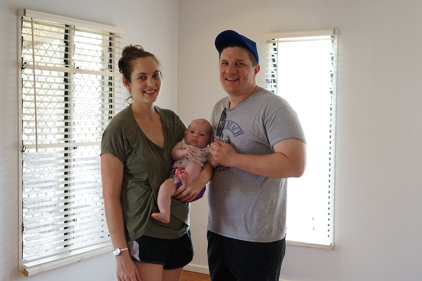 The pair stand with a baby inside the house