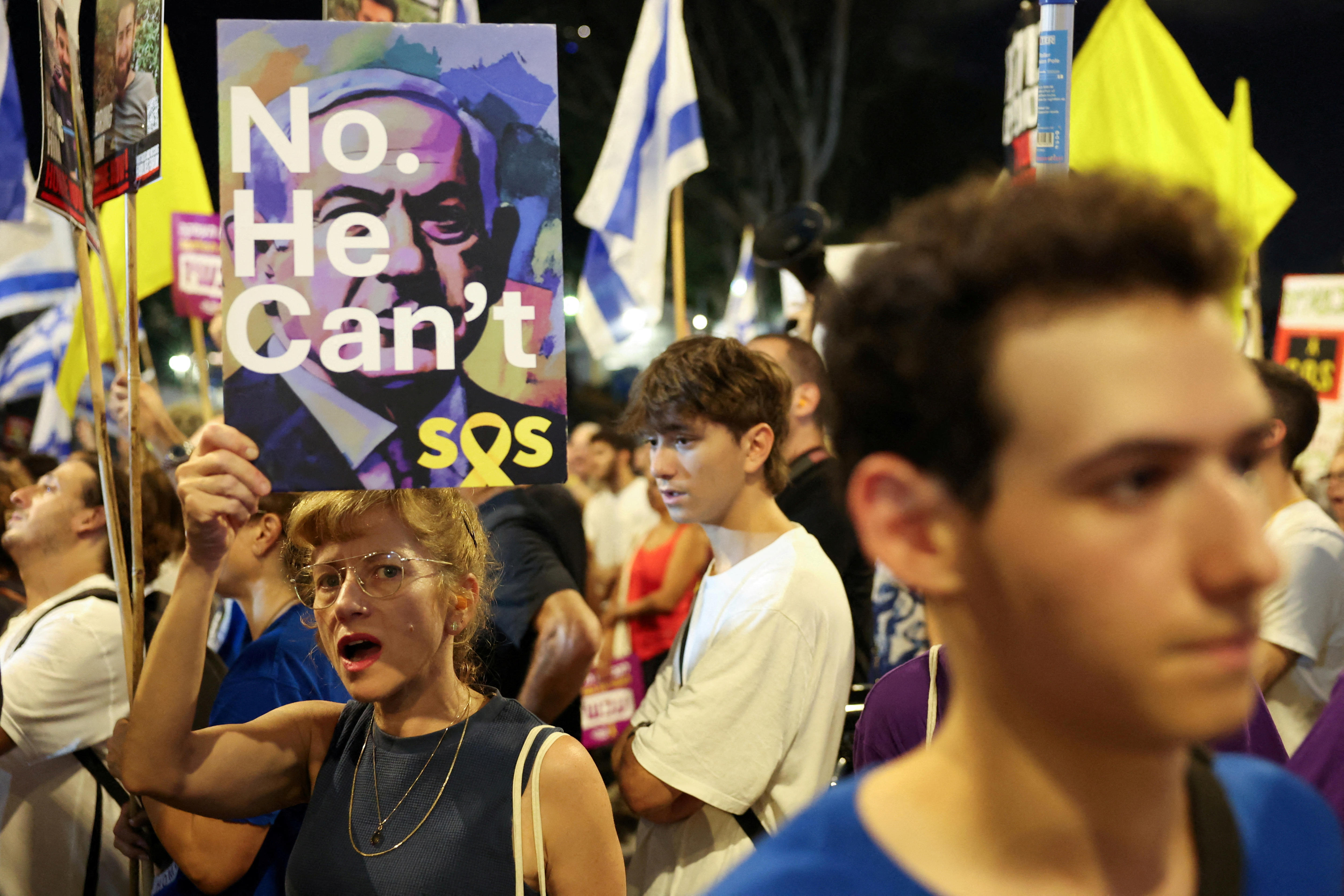 A person surrounded by other protesters holds a sign reading "No. he can't" superimposed on Netanyahu's face