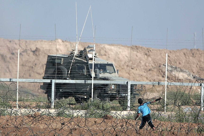 A boy is seen throwing a stone over the fence towards an Israeli military vehicle.