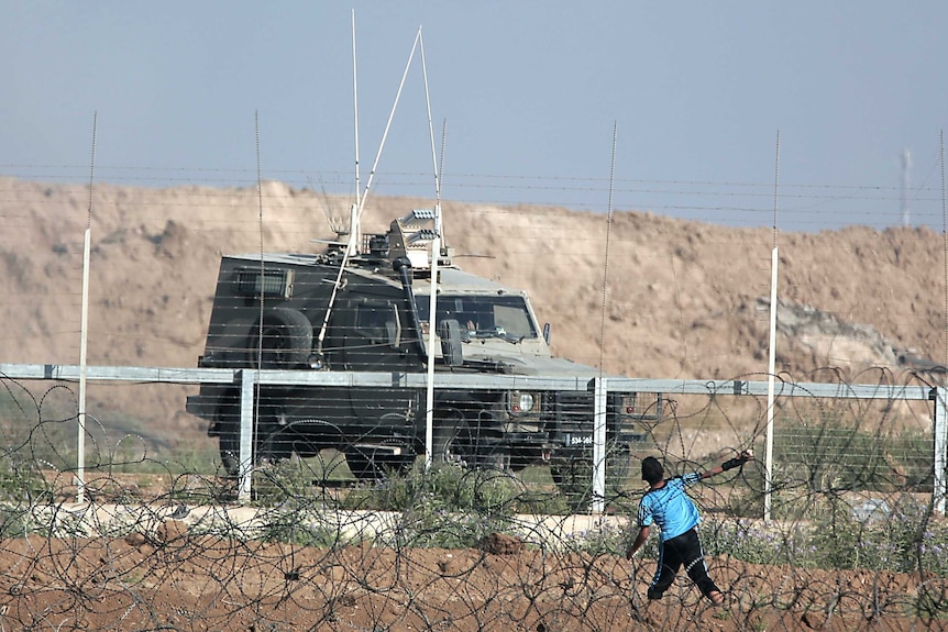 A boy is seen throwing a stone over the fence towards an Israeli military vehicle.