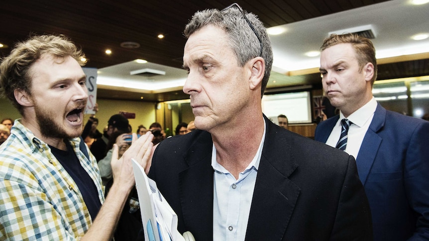 A member of the public clapping closely to a solemn-looking Richard Pearson as he walks out of the meeting.