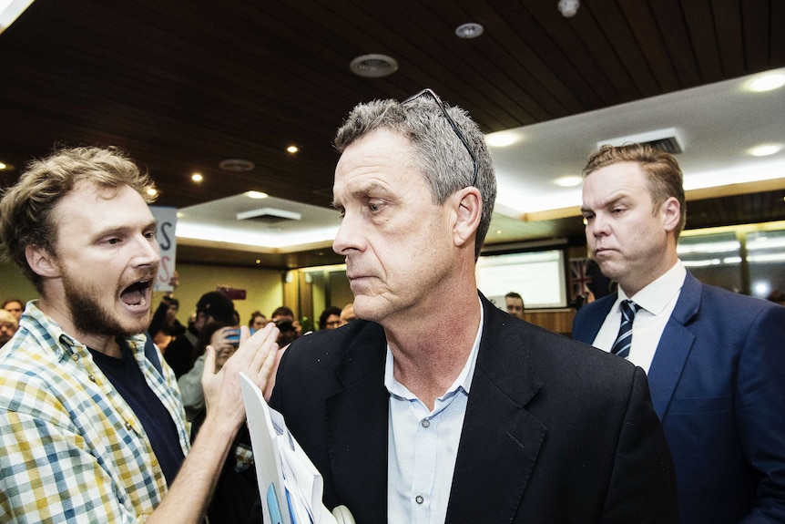 A member of the public clapping closely to a solemn-looking Richard Pearson as he walks out of the meeting.