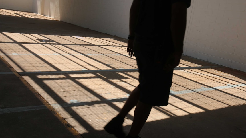 A person in shadow walks through a caged internal courtyard covered in more shadows.