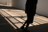 A person in shadow walks through a caged internal courtyard covered in more shadows.