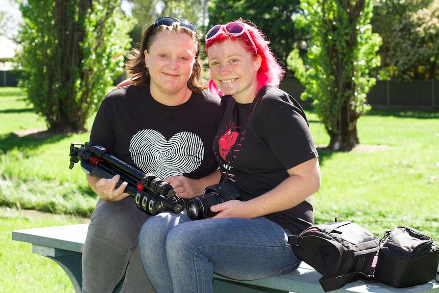 A woman and daughter sitting on a park bench holding photography gear