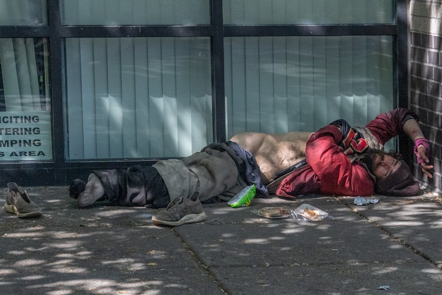 A man lies in the street, his shirt half removed, his shoes scattered.