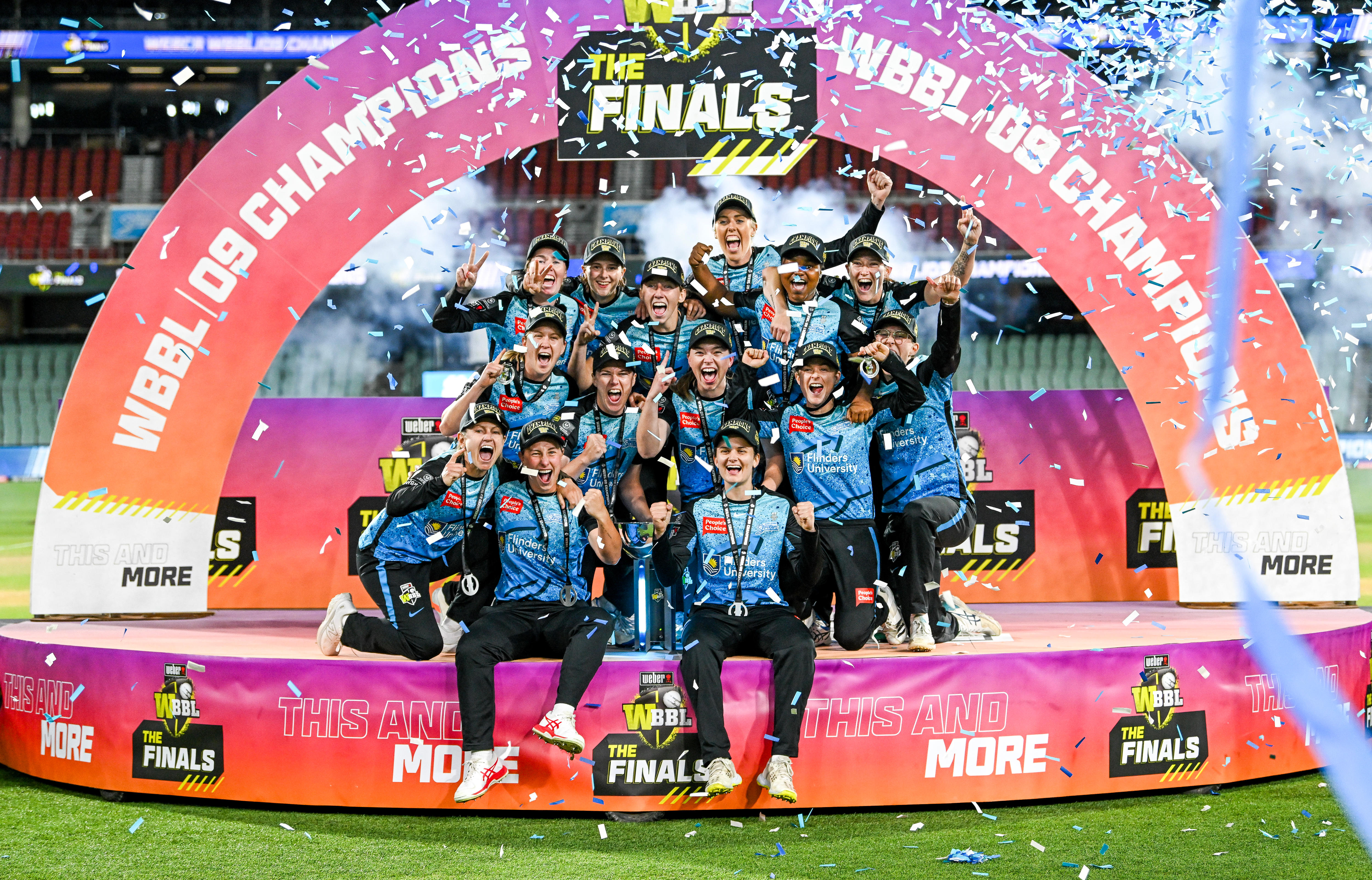 Strikers players huddle together on the podium with the trophy as confetti flies overhead
