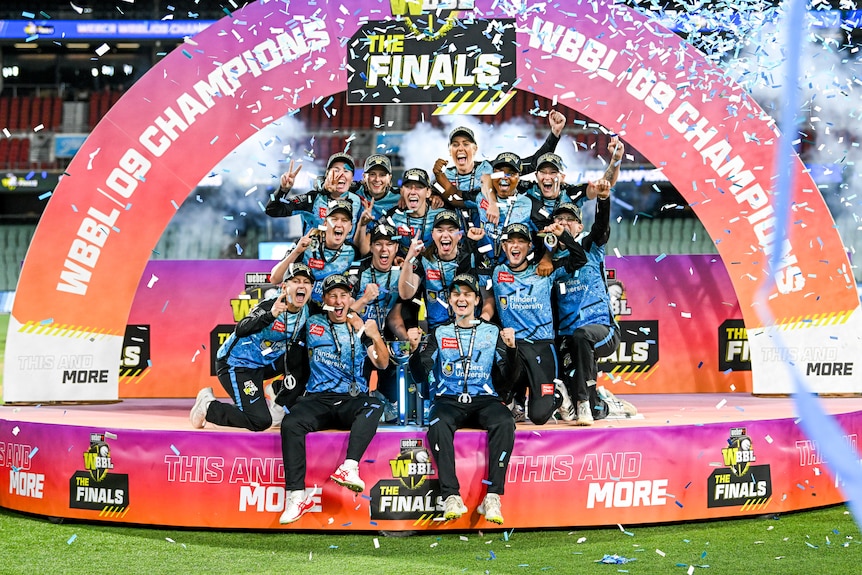 Strikers players huddle together on the podium with the trophy as confetti flies overhead