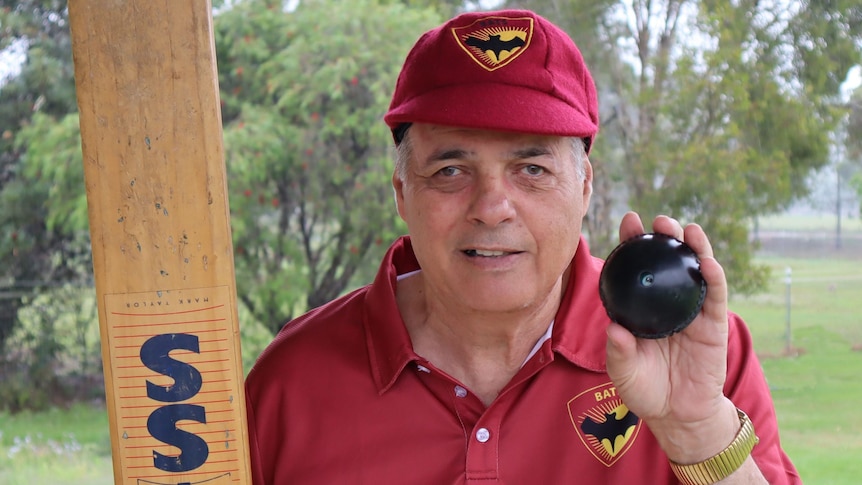 An older man in cricket gear holding a bat and a special ball.