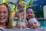 A blonde woman smiles while sitting in the pool with her husband and three small children.