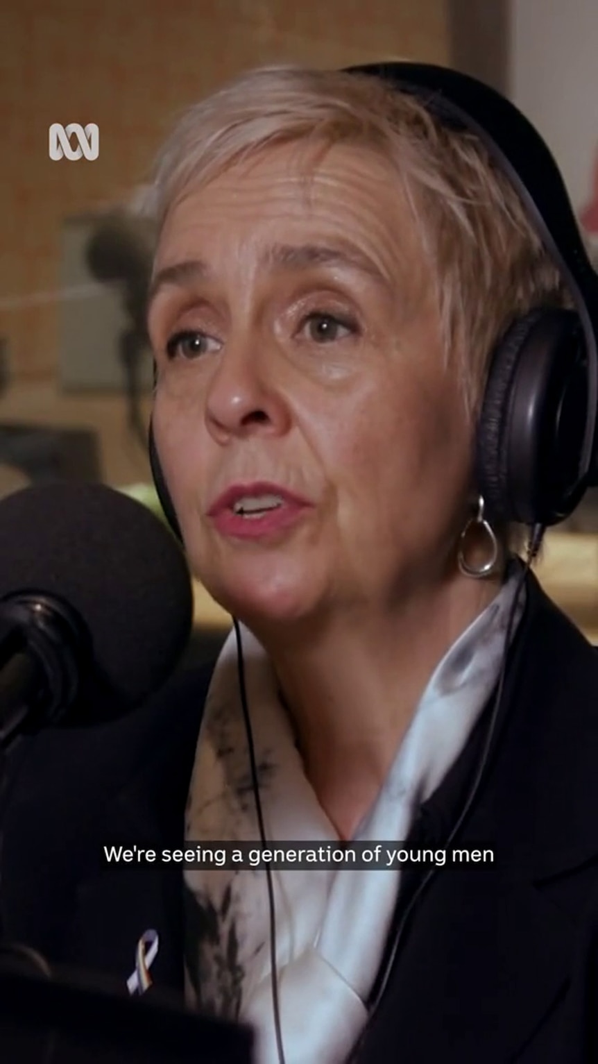 A middle-aged white woman wearing studio headphones with short hair speaks into a microphone