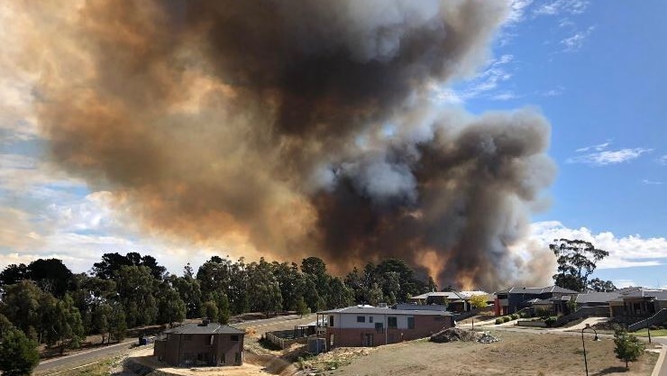 A large plume of smoke rises over homes on a residential street.