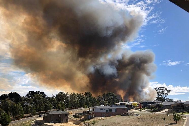 A large plume of smoke rises over homes on a residential street.