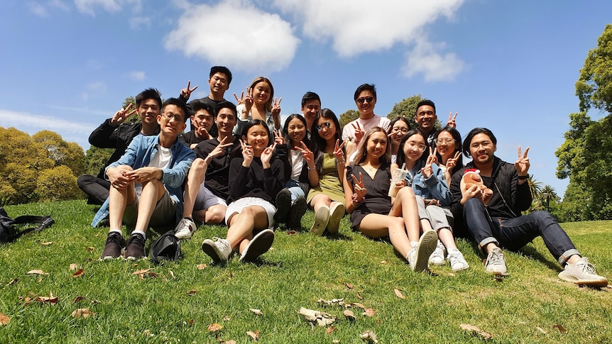 A large group of young Asian people sitting on a green hill on a sunny day