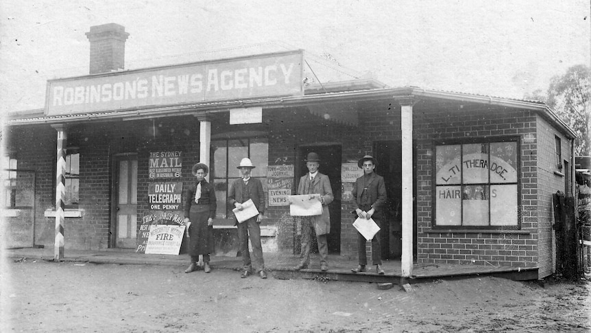 Black and white image of three males and a female in front of a newsagency 