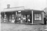 Black and white image of three males and a female in front of a newsagency 