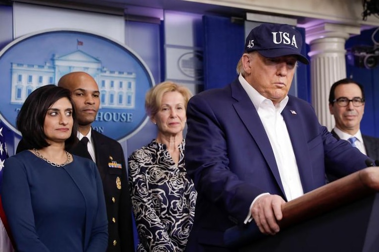 Donald Trump making an announcement wearing a blue camp with USA written on it.