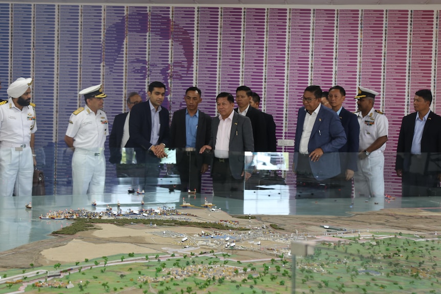 A group of men stand around a table.