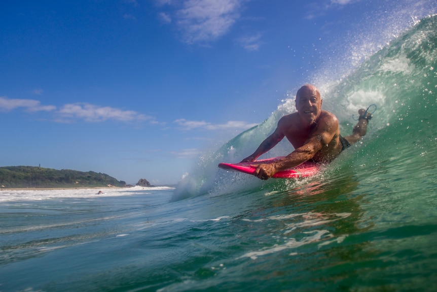 Man catching a wave, gliding through the water on a red board with a big smile on his face