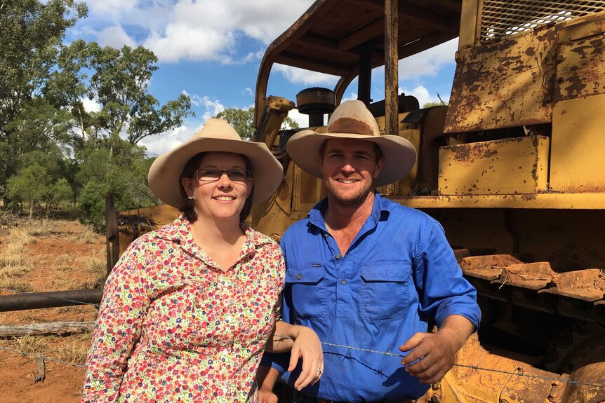 Man and woman wearing akubras stand in front of machinery on a farm