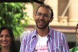 An image of Jonathan Sriranganathan smiling outside city ahll at a press conference with Greens party members behind him 
