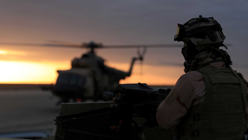 A person dressed in military equipment in front of a helicopter.