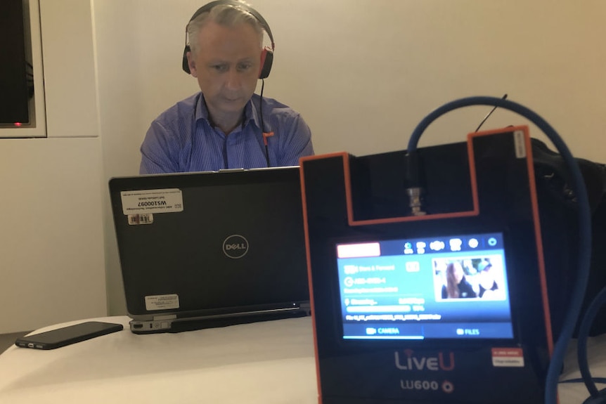 Jennett with headphones on looking at laptop and LiveU unit in foreground with footage on screen.