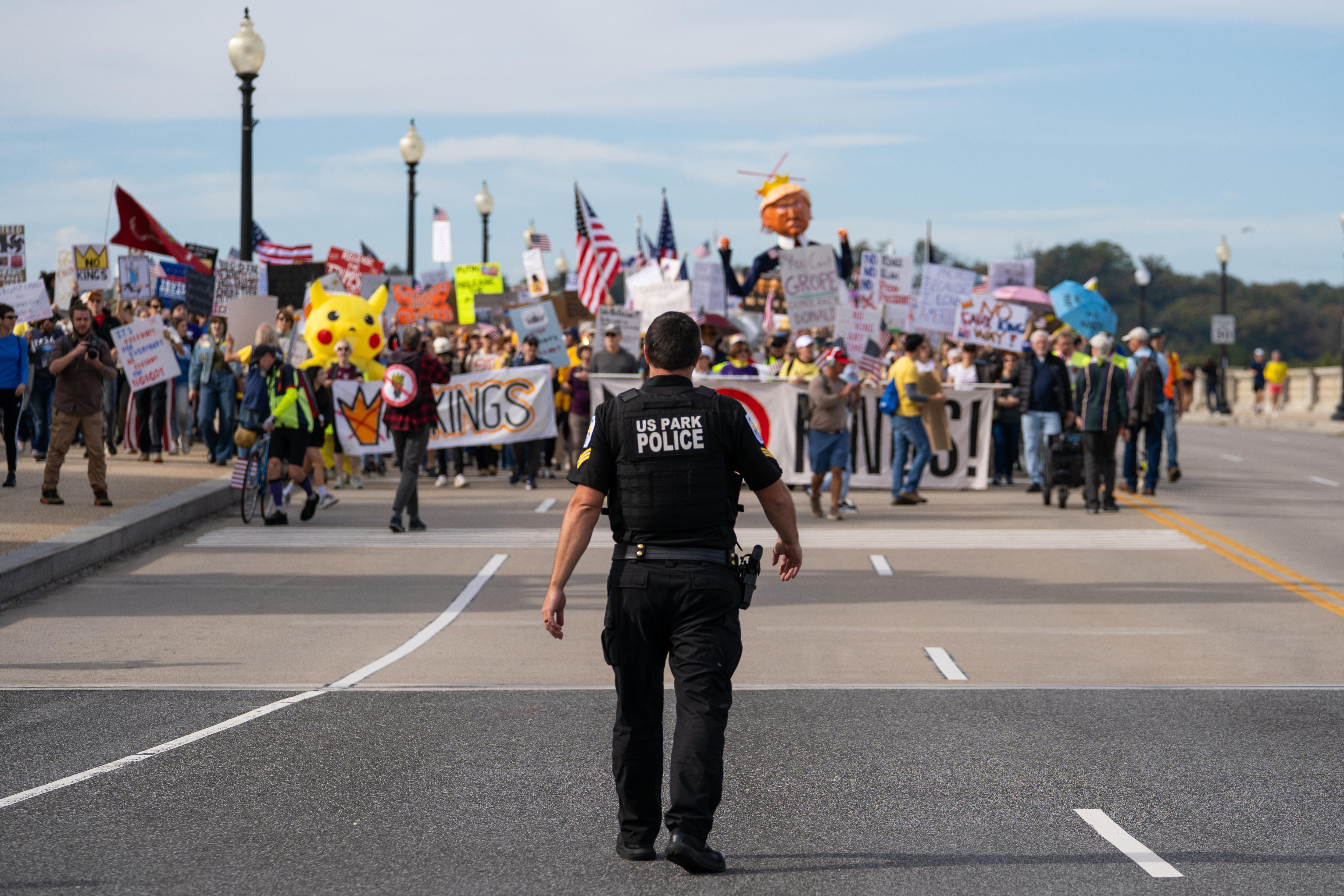 A US Park Police officer in black clothing standing along on a road before a large protest crowd