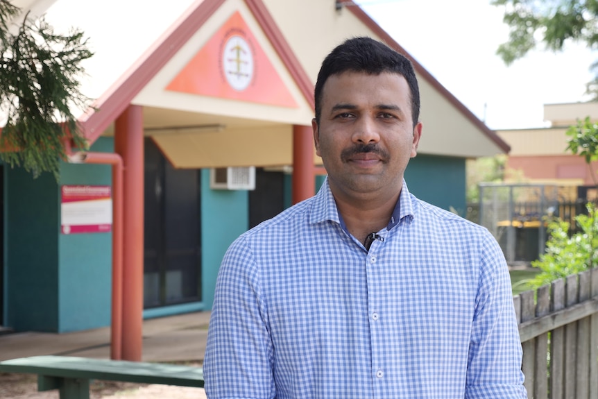 A man in a collared shirt stands in front of a building.