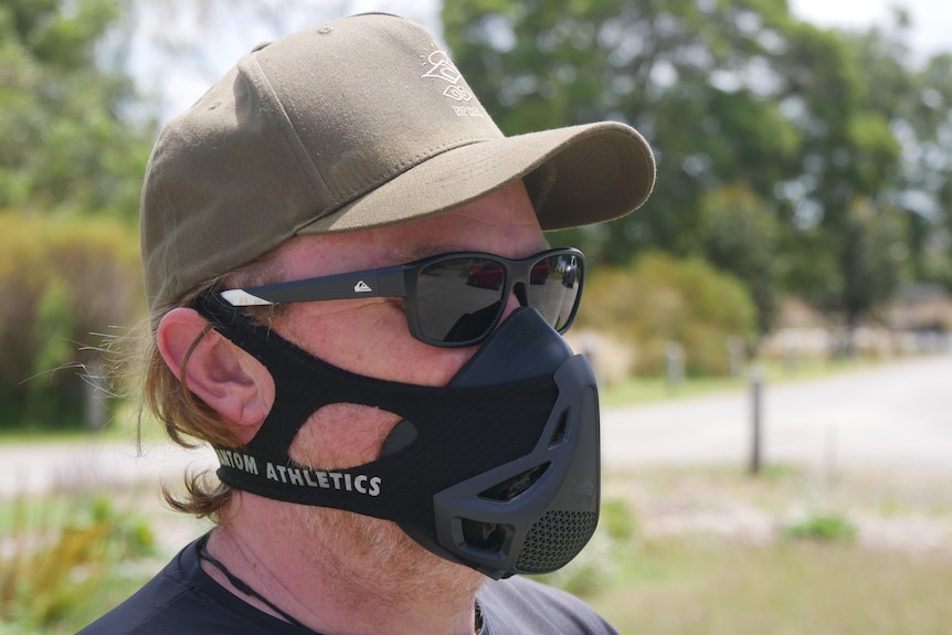 A man looking to the right while wearing an altitude mask, glasses and a hat.