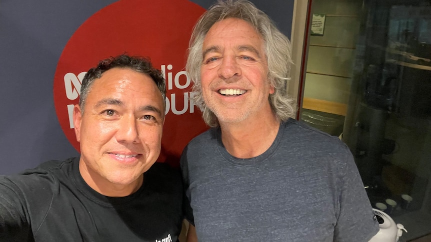 A selfie of two men smiling and looking at the camera in a radio studio