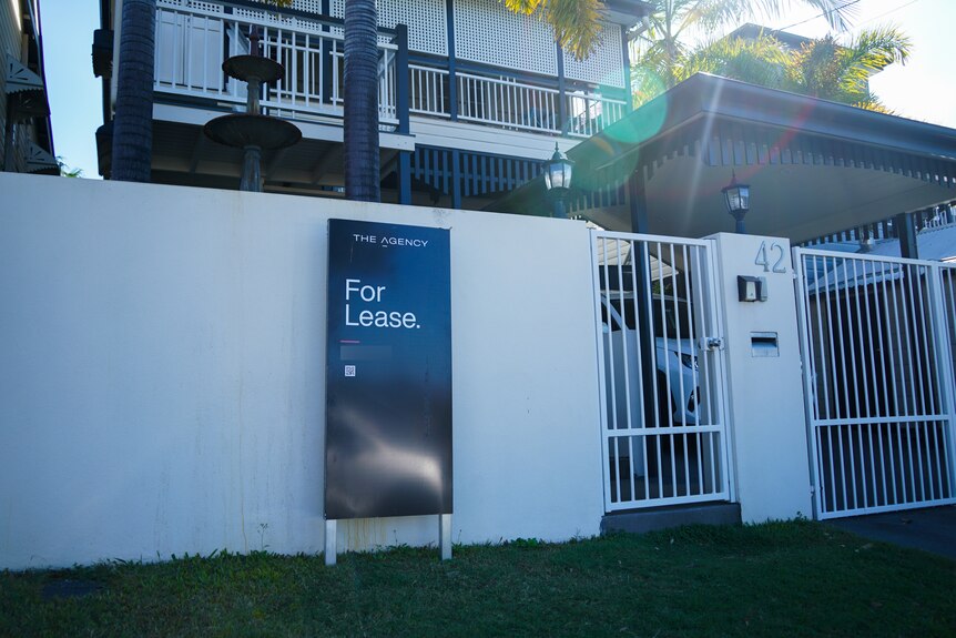 A 'for lease' real estate sign sits outside the front fence of a home