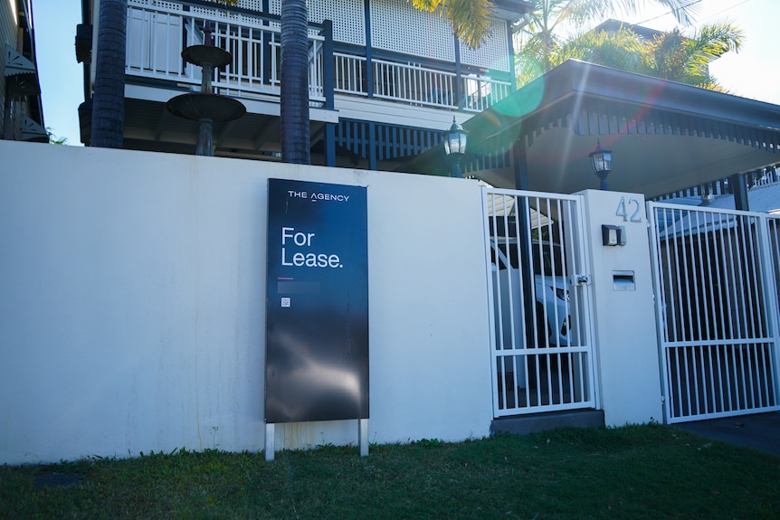 A 'for lease' real estate sign sits outside the front fence of a home