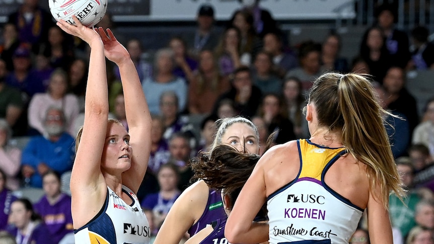Steph Wood holds a netball above her head with three other women in front of her