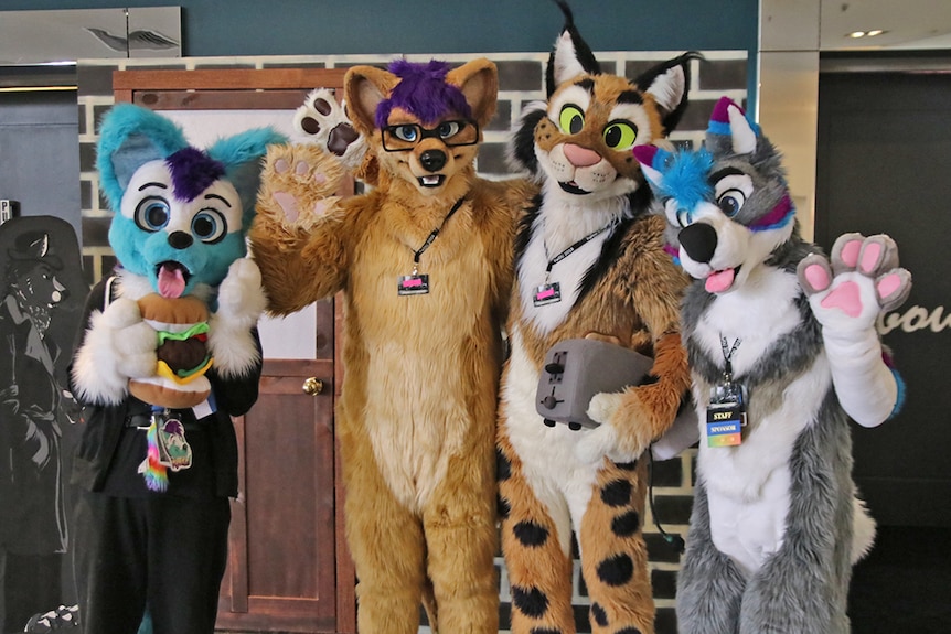 Four people dressed in furry animal costumes with their arms around each other's shoulders